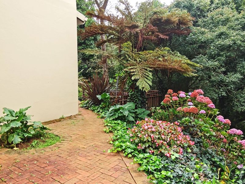 A well-maintained garden area featuring brick paving and established landscaping alongside the side of the house.