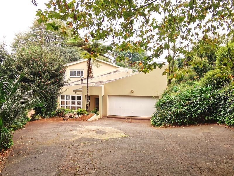 Front elevation of a residential property featuring a paved driveway, double garage, and established garden surroundings.