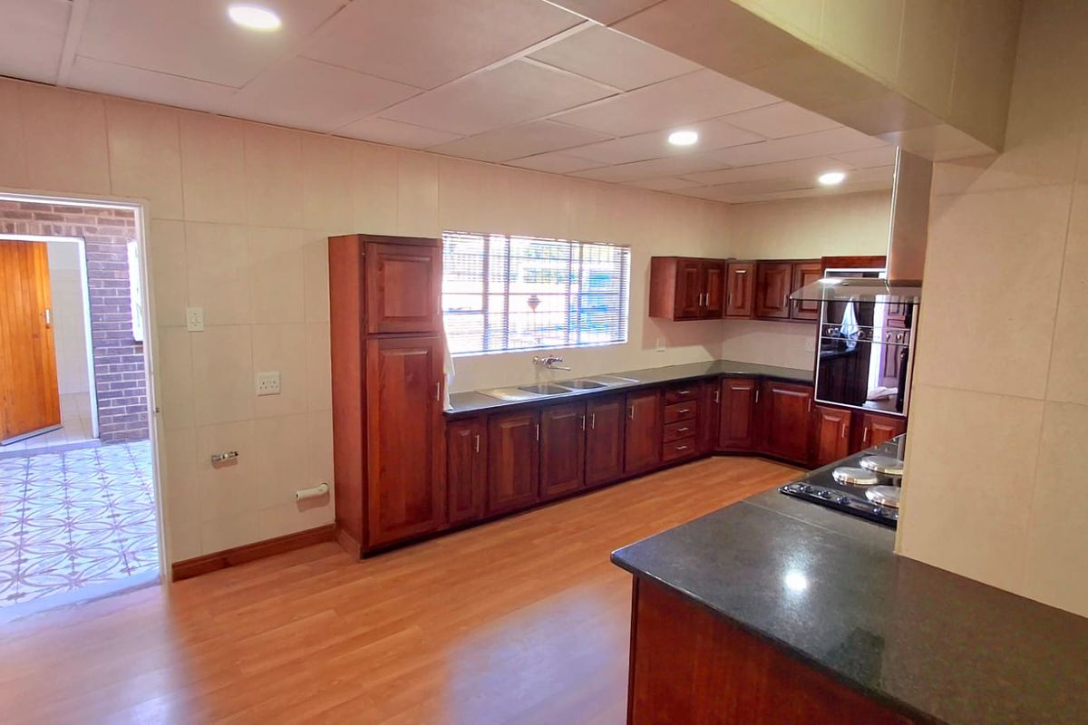 Spacious kitchen featuring extensive wooden cabinetry, dark stone countertops, built-in oven, extractor fan, and tiled wall finishes.