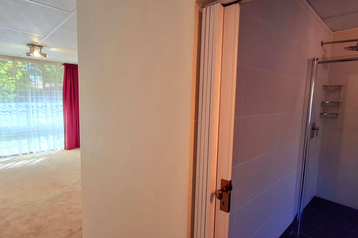 A bathroom featuring a shower enclosure with tiled walls, adjacent to a carpeted living area with large windows.