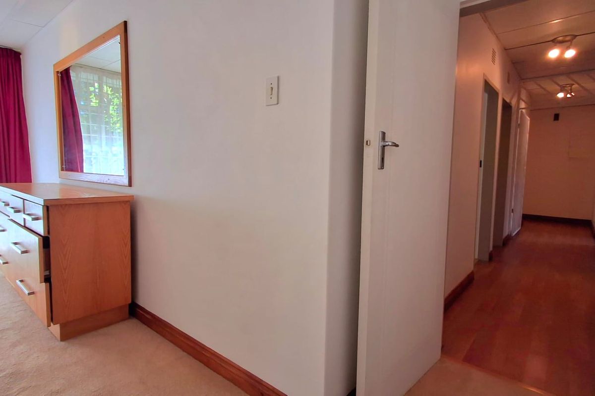 A bedroom interior featuring timber skirting boards and an open doorway leading into a hallway with wooden flooring and ceiling lighting.