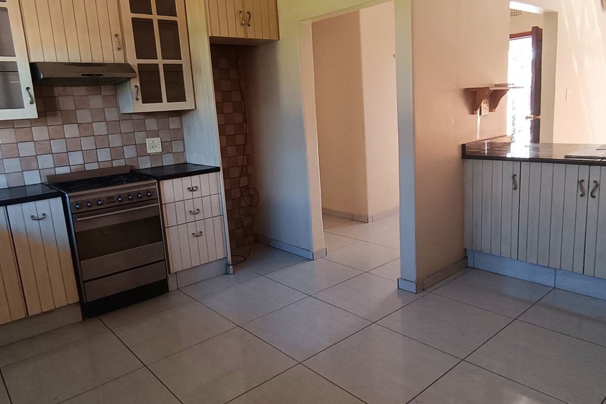 A functional kitchen featuring light-toned cabinetry, a built-in oven with extractor fan, dark countertops, and tiled flooring, offering a practical layout for daily use.