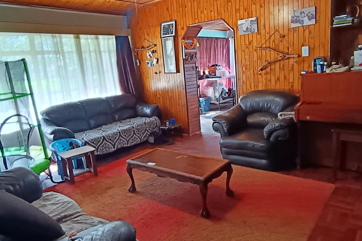 A living room featuring traditional timber wall paneling, a timber ceiling, and parquet flooring, with an archway leading to an adjacent space.
