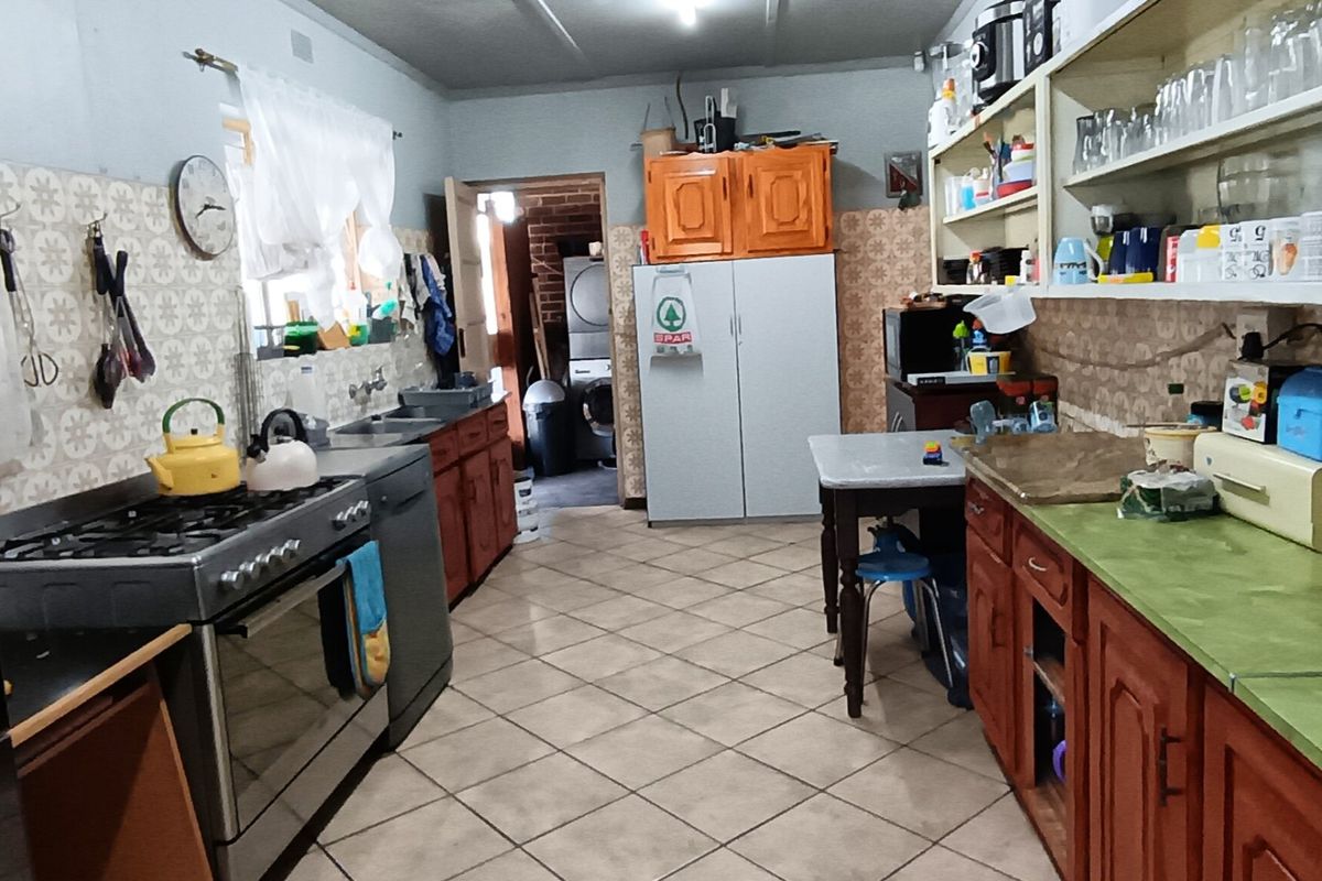 A functional kitchen featuring a gas stove, double sink, tiled flooring, and ample built-in cabinetry with open shelving for storage.