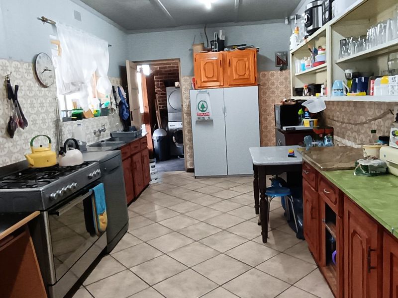 A functional kitchen featuring a gas stove, double sink, tiled flooring, and ample built-in cabinetry with open shelving for storage.