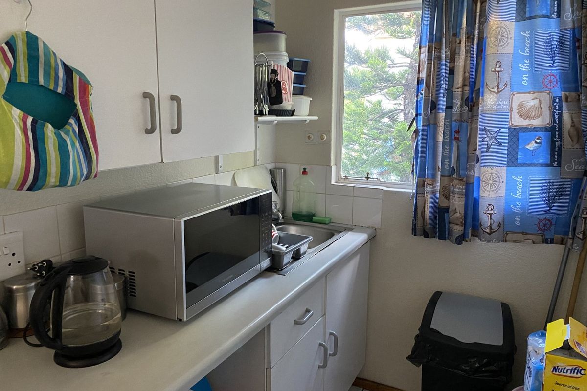 Compact kitchen featuring white cabinetry, laminate countertops, a stainless steel sink, and a tiled backsplash, providing a functional workspace.