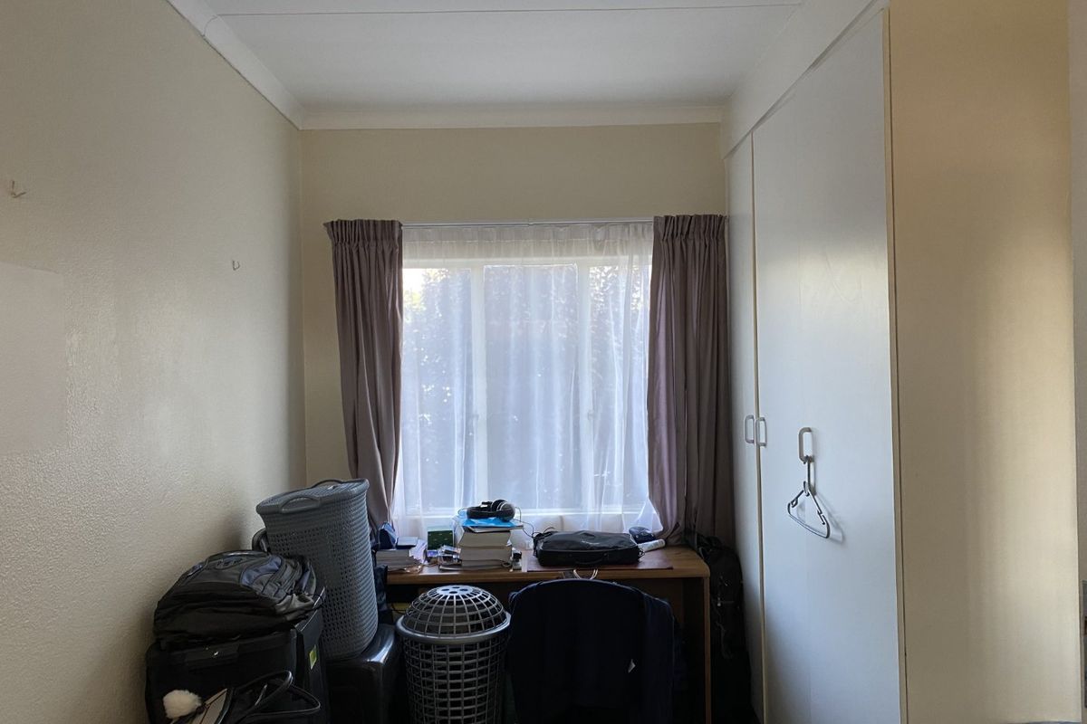 A bedroom featuring built-in cupboards and a window with curtains, providing a functional space with potential for modernization.