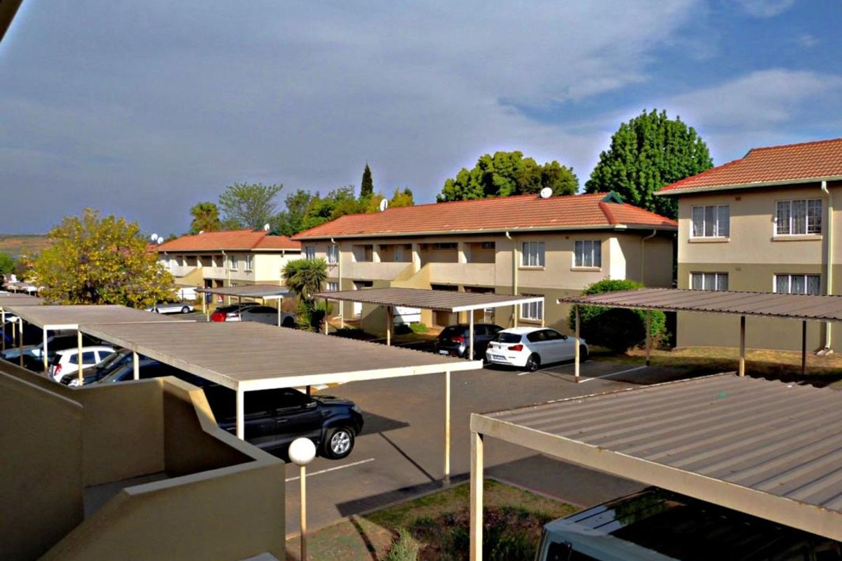 An elevated view of the apartment complex exterior, featuring multiple carports, paved parking areas, and residential building blocks with tiled roofs.