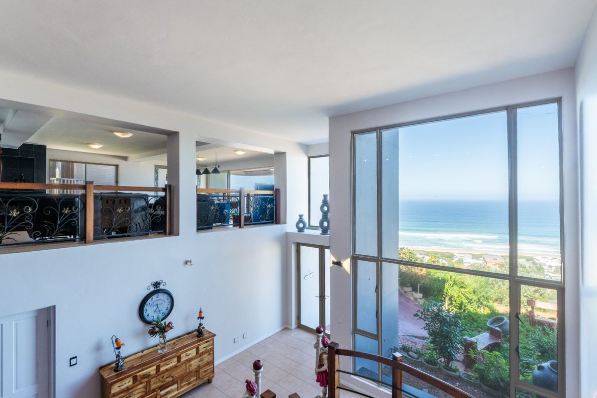 Spacious double-volume living area featuring expansive windows with panoramic ocean views and a mezzanine level with decorative wrought iron railings.