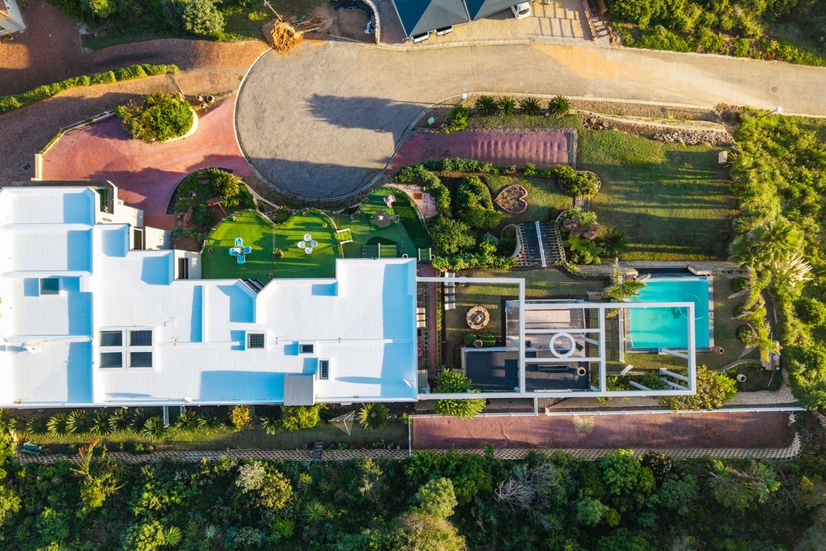 Aerial view of the property showcasing the main dwelling, swimming pool, landscaped garden areas, and paved driveway access.