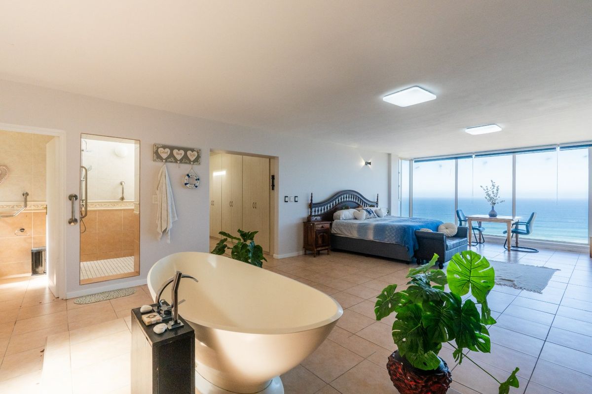 Spacious open-plan bedroom featuring a freestanding bathtub, en-suite walk-in shower, built-in storage, and expansive floor-to-ceiling windows with panoramic ocean views.