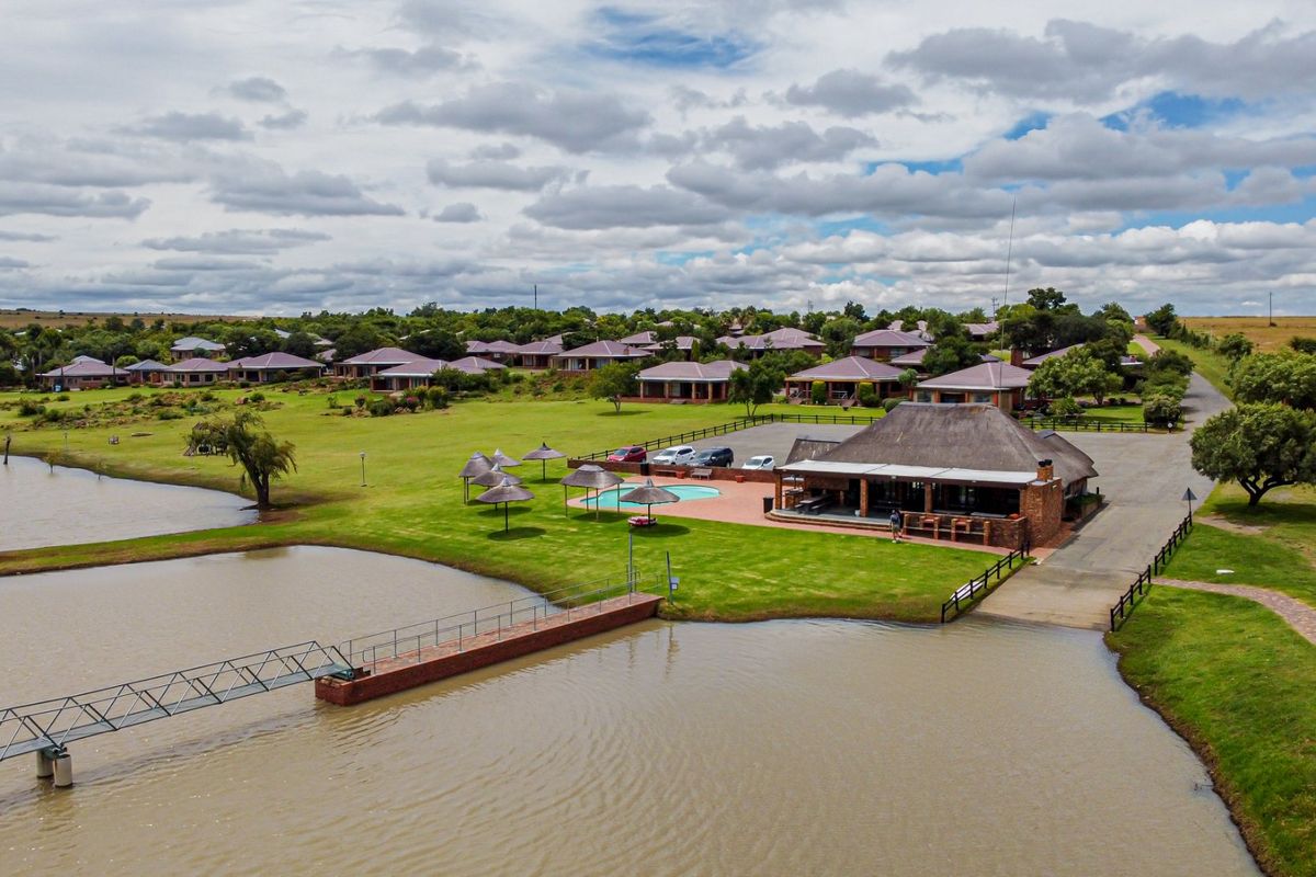 Aerial view of a residential estate featuring a clubhouse, swimming pool, and a private jetty extending into the lake.