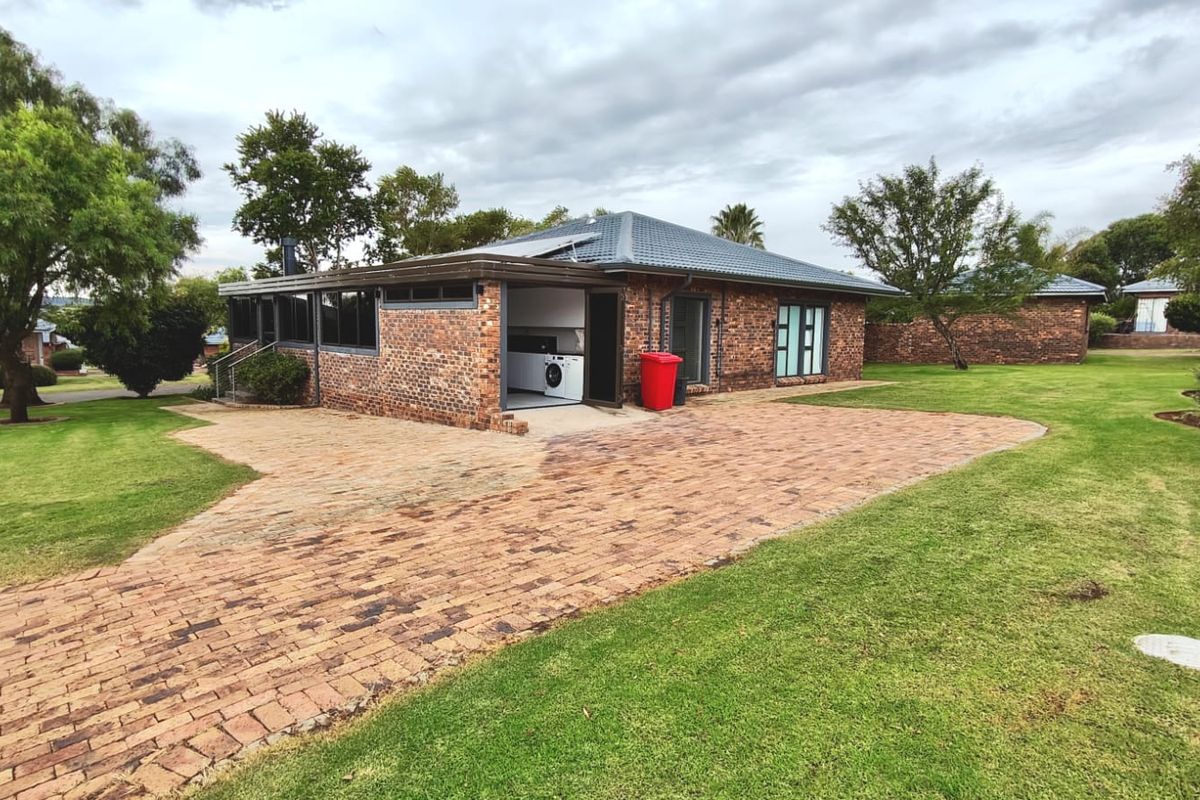 Rear view of a brick house featuring a paved driveway, landscaped garden, and solar water heating system on the tiled roof.