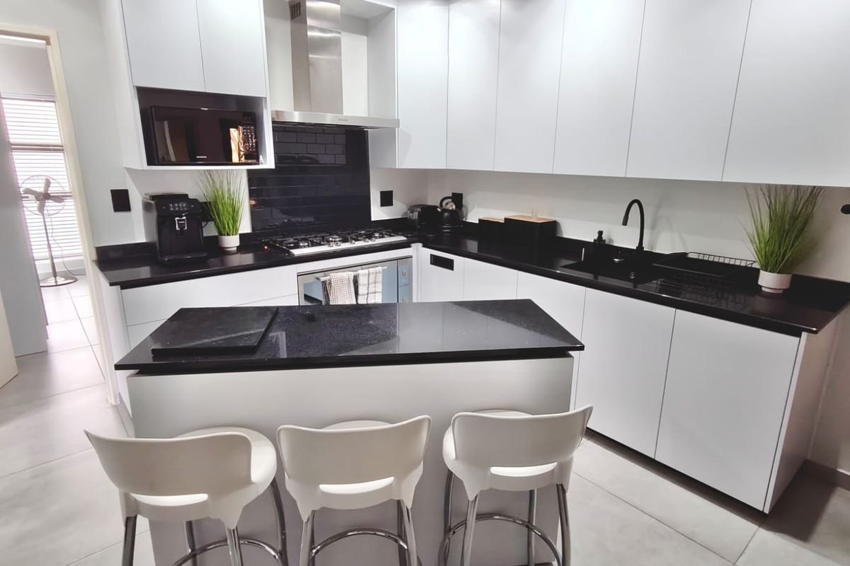 Modern kitchen featuring sleek white cabinetry, contrasting black granite countertops, gas hob, extractor fan, and high-quality finishes throughout.