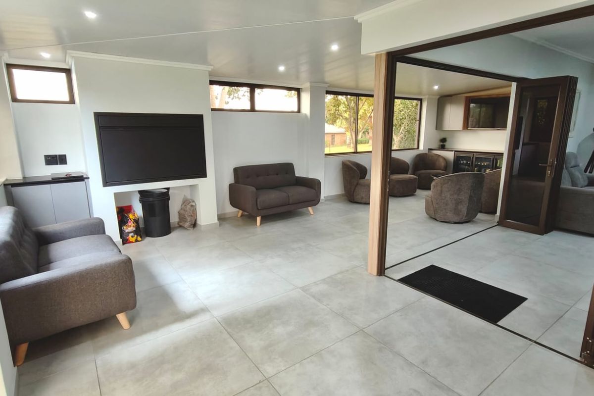 Spacious living area featuring large format floor tiles, recessed lighting, a built-in fireplace, and seamless access to an adjacent bar area through sliding doors.
