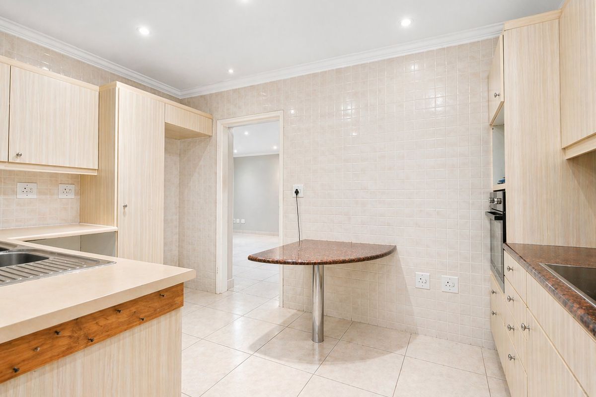 A functional kitchen featuring light wood cabinetry, tiled walls, a built-in oven, and a compact breakfast nook area.
