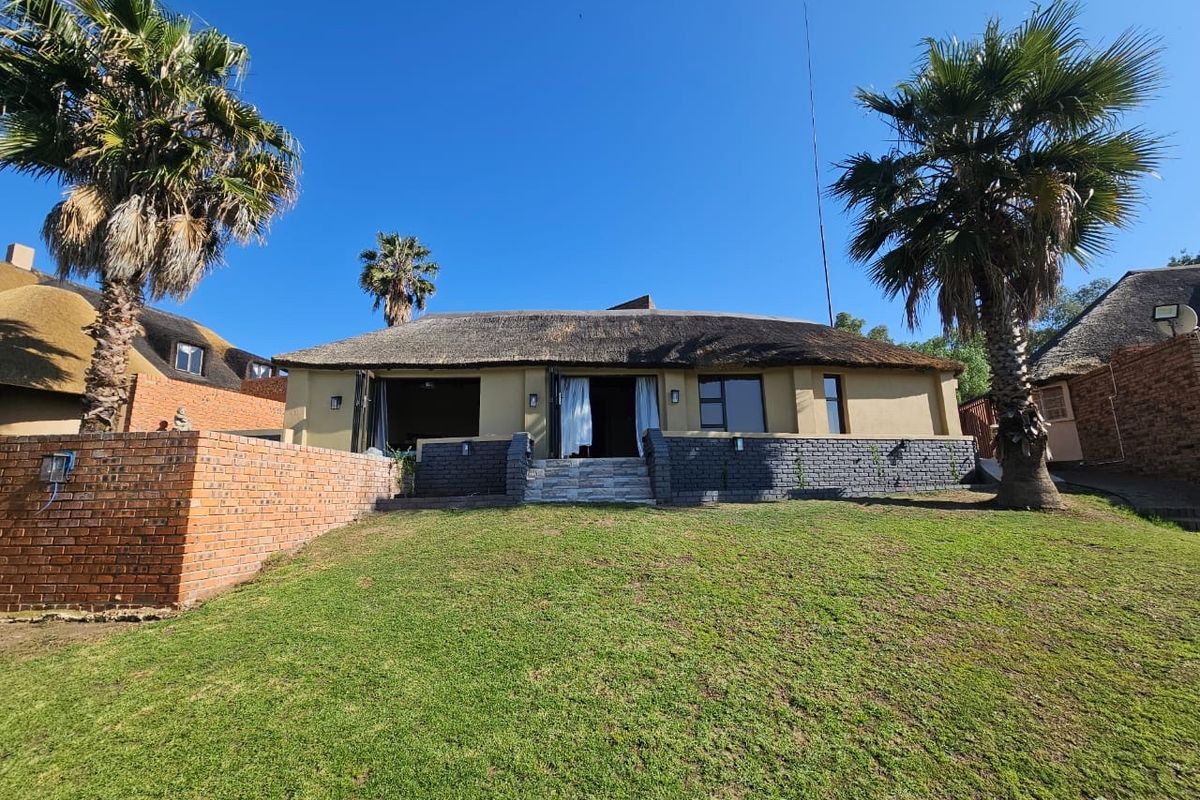 Rear view of a thatched-roof house featuring a landscaped lawn, brick retaining walls, and bi-fold doors leading to the interior.