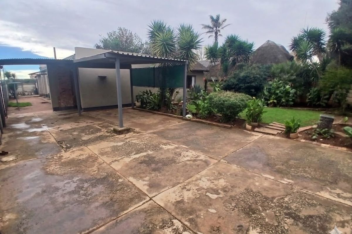 Rear exterior area featuring a covered patio structure and concrete paving leading to a garden space.