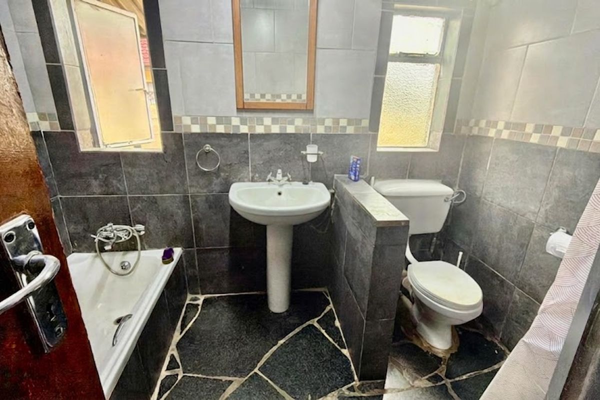 A functional bathroom featuring a pedestal basin, toilet, and bathtub with dark tiled walls and flooring, offering a dated but practical layout.