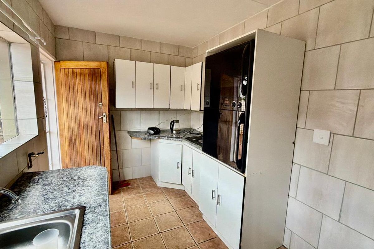 A functional kitchen featuring built-in cabinetry, granite countertops, a stainless steel sink, and a built-in oven with tiled wall and floor finishes.