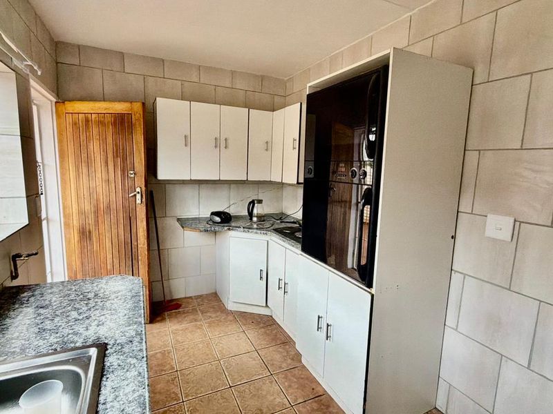 A functional kitchen featuring built-in cabinetry, granite countertops, a stainless steel sink, and a built-in oven with tiled wall and floor finishes.