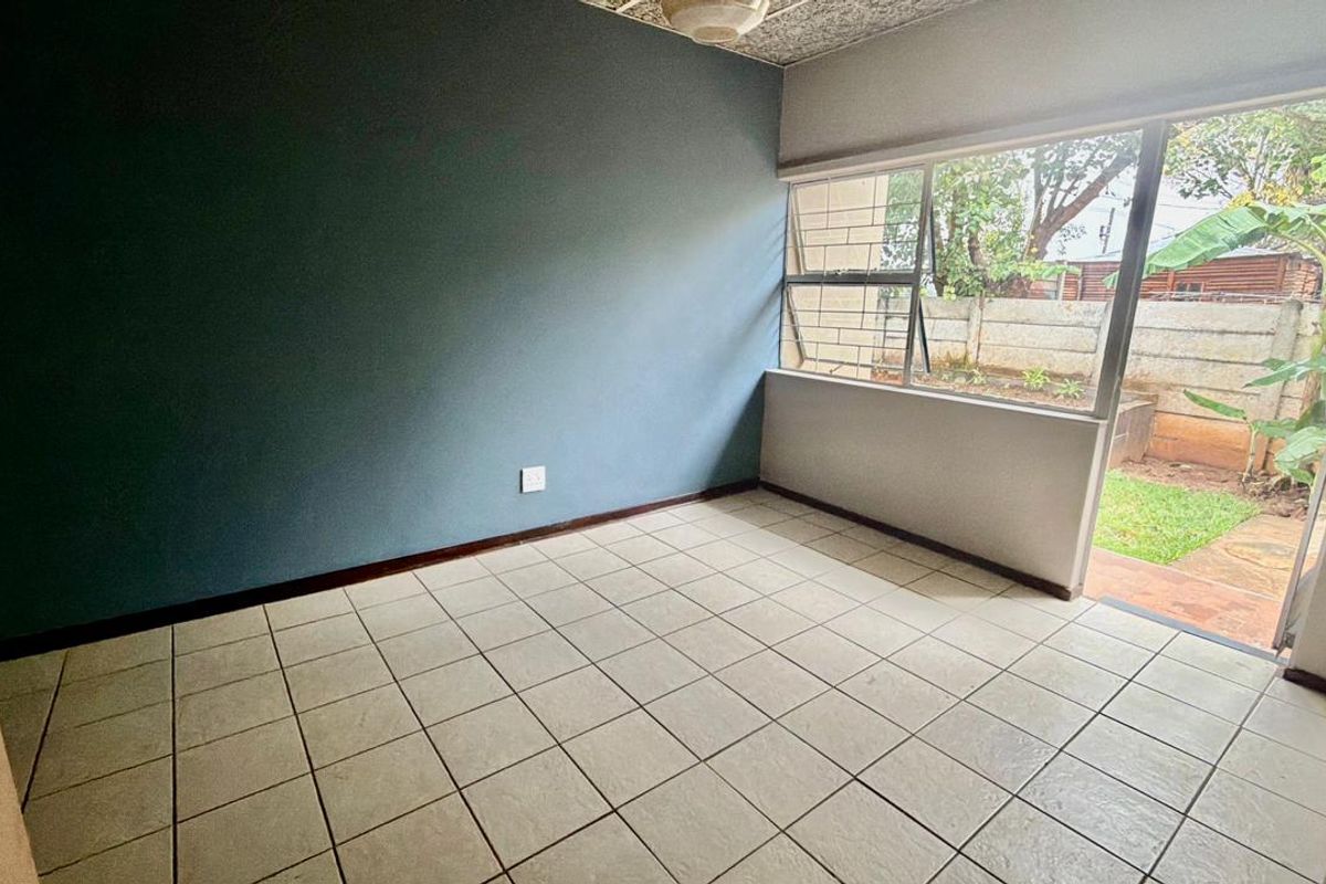 An empty bedroom featuring tiled flooring, a textured ceiling, and a large window with direct access to the garden area.