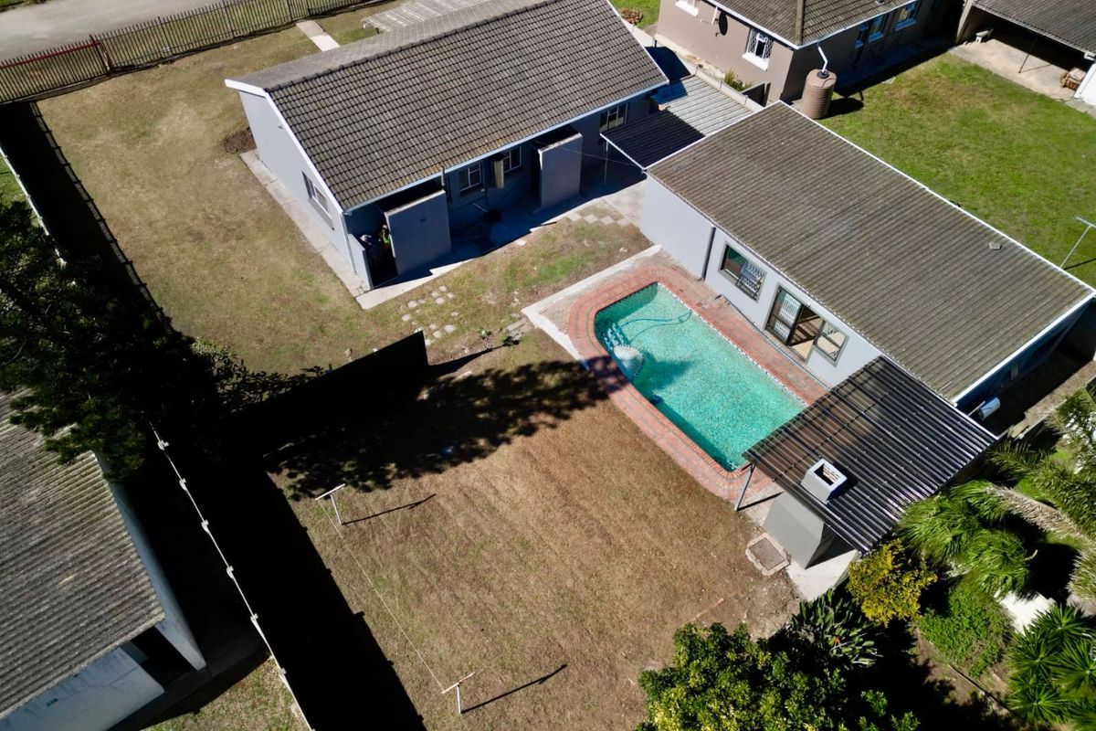 Aerial view of a residential property featuring a swimming pool, covered patio area, and surrounding garden space with perimeter fencing.