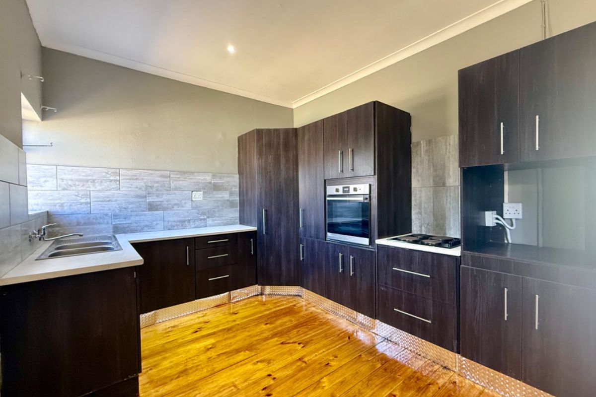 A functional kitchen featuring dark wood cabinetry, built-in oven, hob, tiled backsplash, and timber flooring, offering a clean and practical workspace.