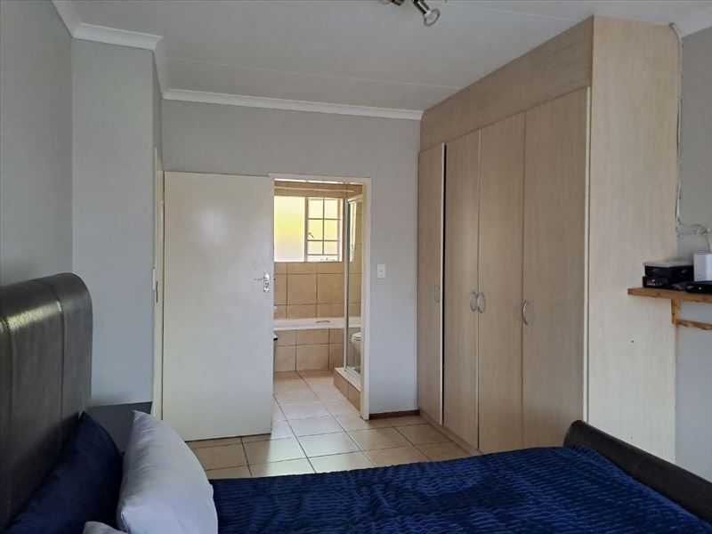 A bedroom featuring built-in cupboards and an adjoining en-suite bathroom with tiled flooring and neutral wall finishes.