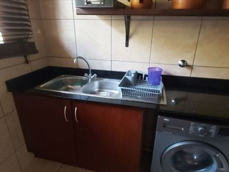 A functional scullery area featuring a double basin sink, granite countertops, tiled splashbacks, and dedicated space for a washing machine.