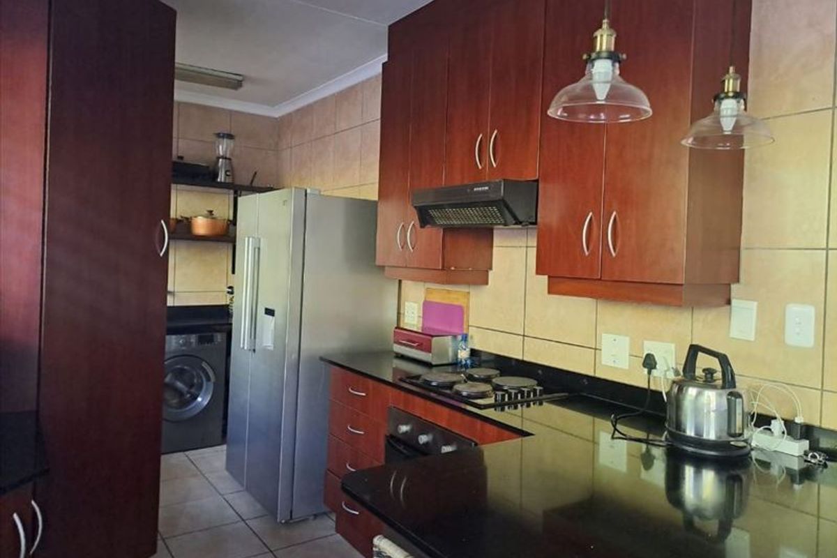 A functional kitchen featuring dark wood cabinetry, granite countertops, an integrated hob and oven, and tiled wall finishes.