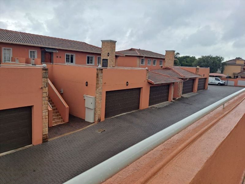 An elevated view of a townhouse complex featuring multiple garages, brick-paved driveway, and terracotta-toned exterior walls with stone cladding accents.