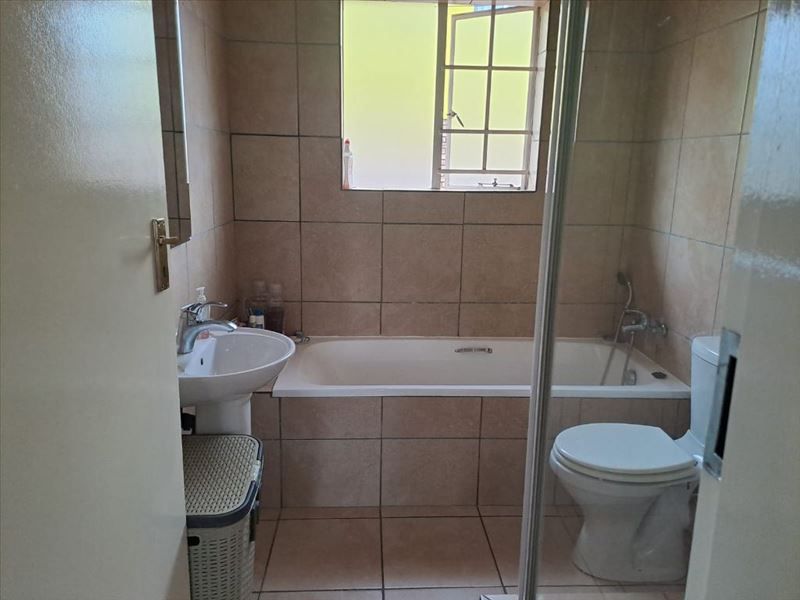A functional bathroom featuring a pedestal basin, built-in bathtub, toilet, and shower screen with neutral wall and floor tiling.