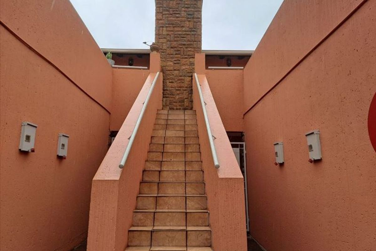 Exterior view of a townhouse featuring a central stone chimney and a tiled staircase leading to an upper level.