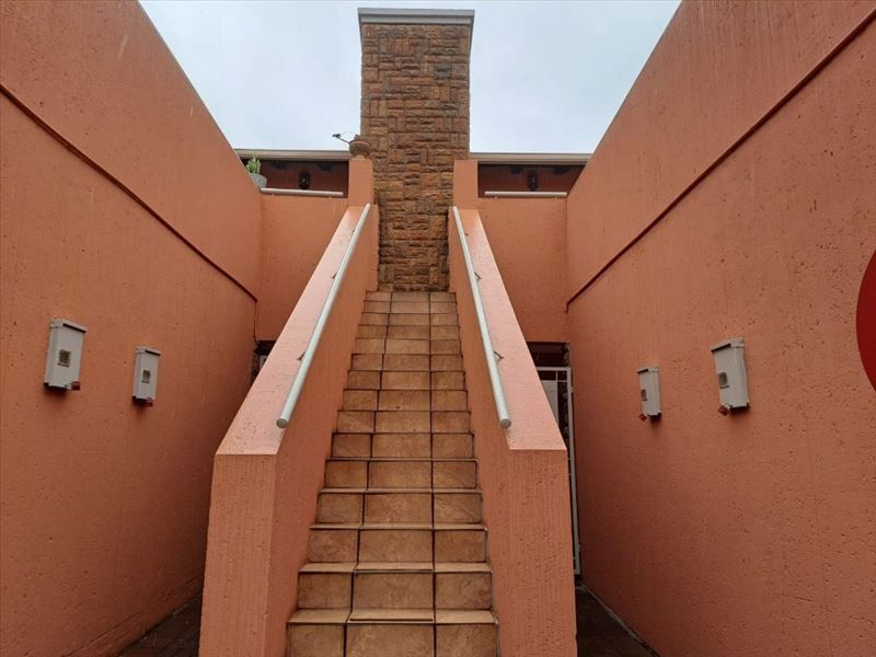 Exterior view of a townhouse featuring a central stone chimney and a tiled staircase leading to an upper level.