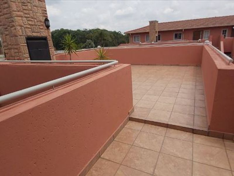 A spacious open-air rooftop balcony featuring tiled flooring, masonry walls with metal handrails, and a prominent stone-clad chimney stack.