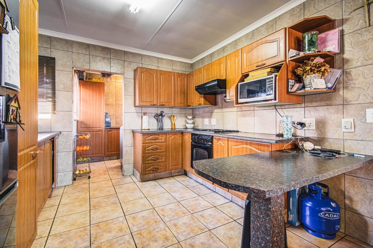 A functional kitchen featuring wood-finish cabinetry, tiled walls and flooring, a built-in oven, and a breakfast bar, with an adjacent scullery area.