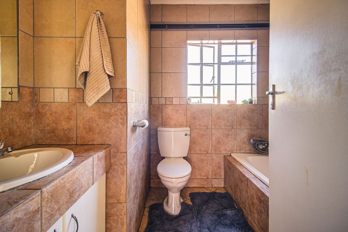 A functional bathroom featuring a built-in vanity with basin, a standard toilet, and a tiled bathtub surround with a window.