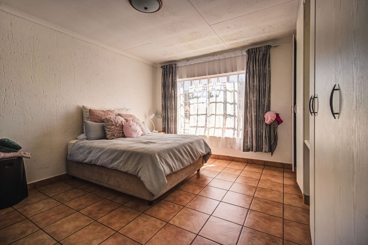 A bedroom featuring tiled flooring, built-in cupboards, and a large window allowing natural light.