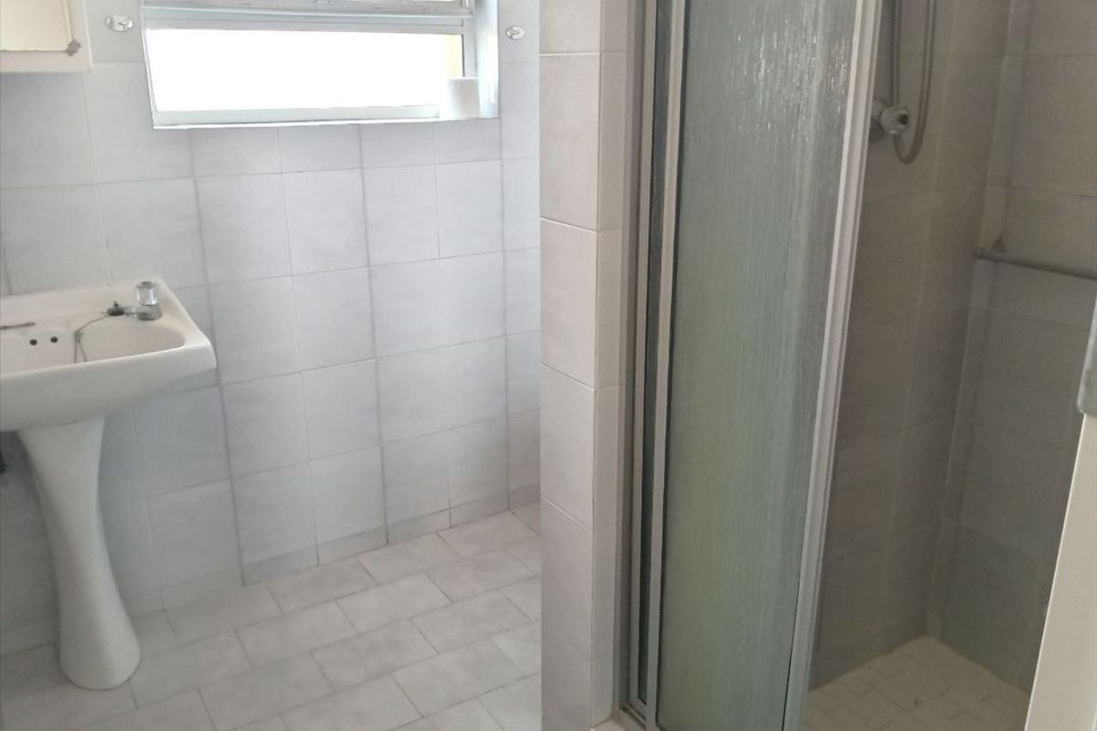 A functional bathroom featuring a pedestal basin, tiled finishes, and a glass-enclosed shower unit.