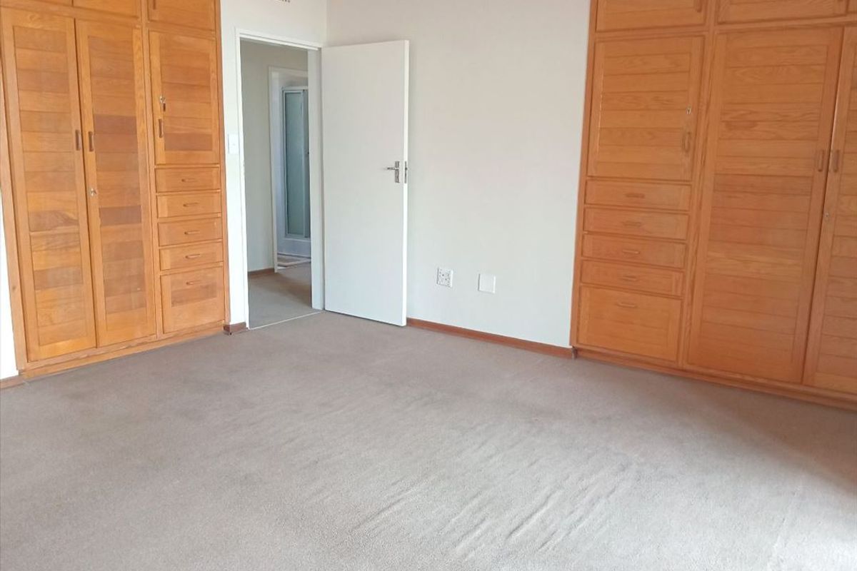 A spacious bedroom featuring extensive built-in wooden cabinetry and neutral carpeting, offering a blank canvas for interior design updates.