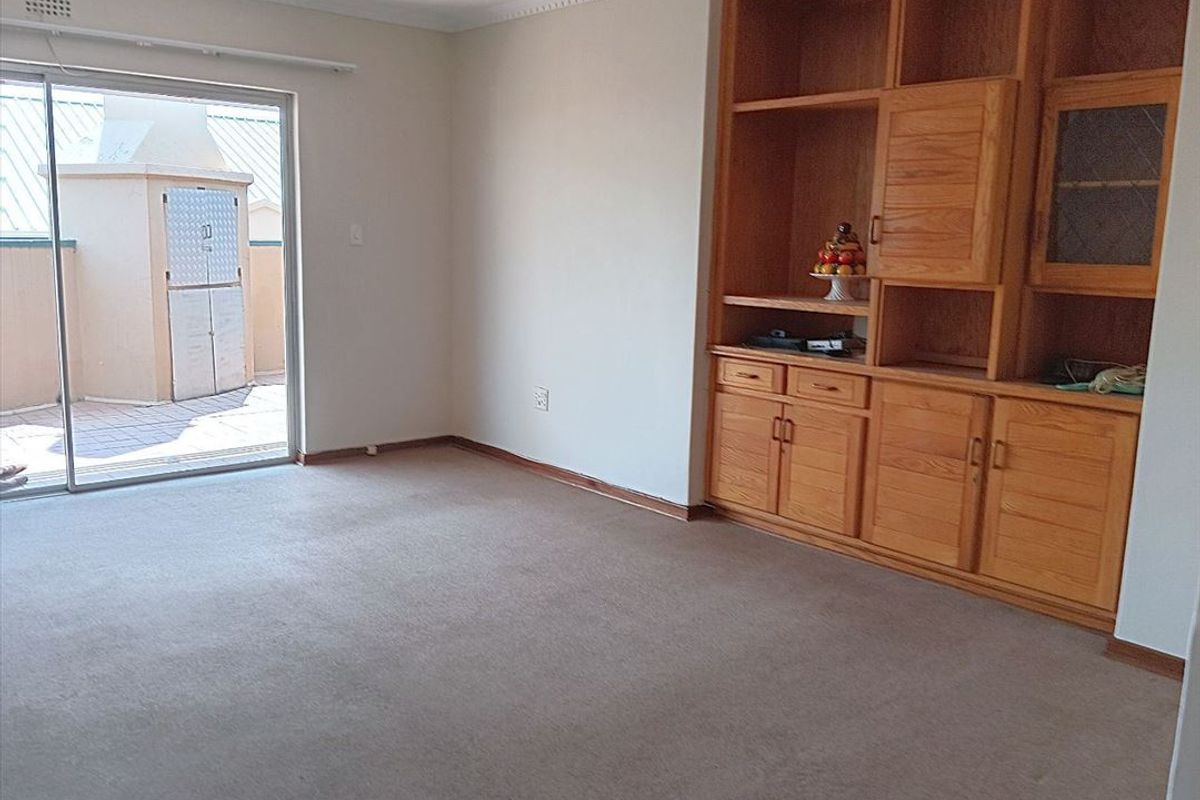Spacious living room featuring built-in wooden cabinetry, carpeted flooring, and a sliding glass door providing access to an outdoor patio area.
