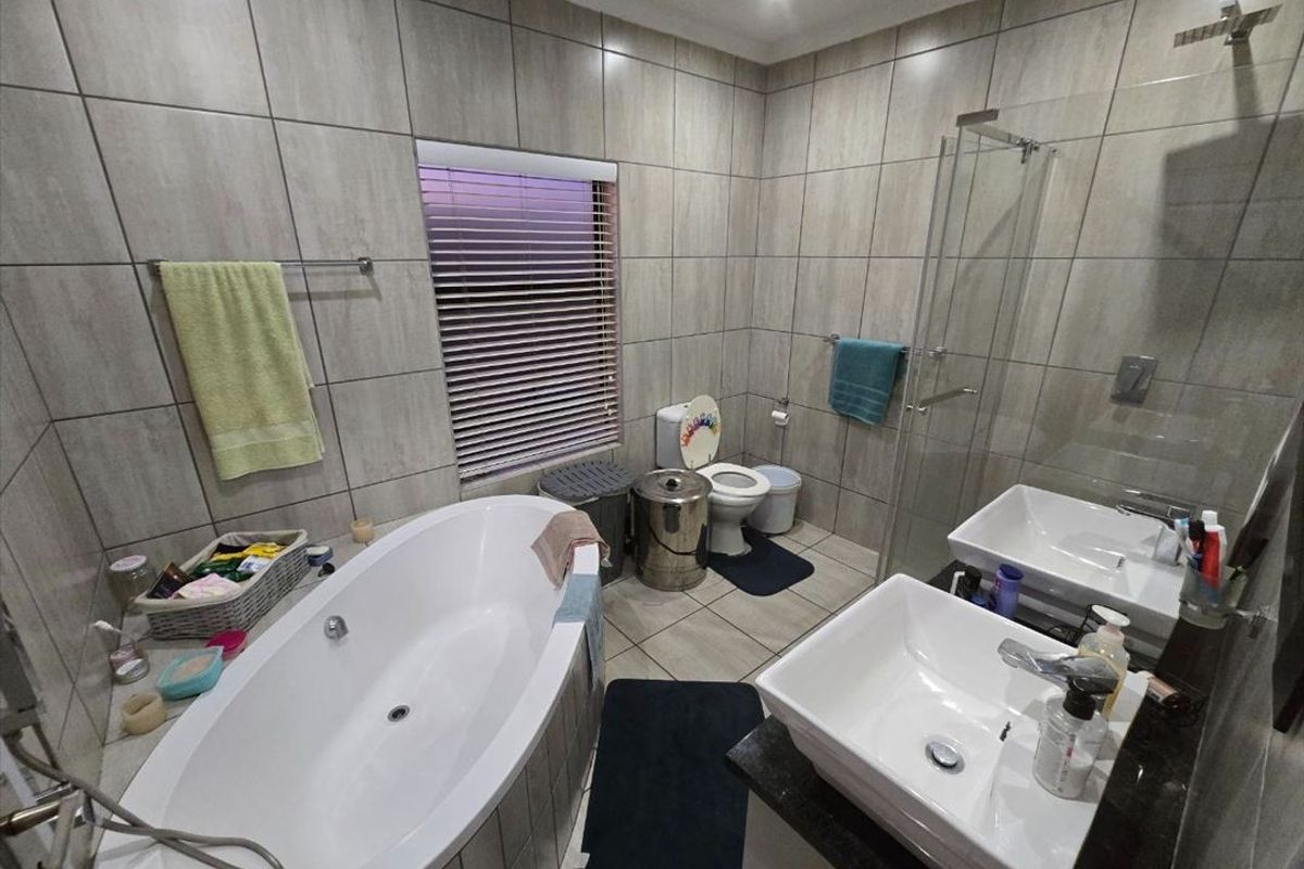 Modern bathroom featuring a freestanding bathtub, double vanity with vessel sinks, and a glass-enclosed shower with floor-to-ceiling tiling.