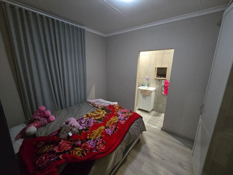 A bedroom featuring laminate flooring and an en-suite bathroom with a vanity basin and tiled walls.