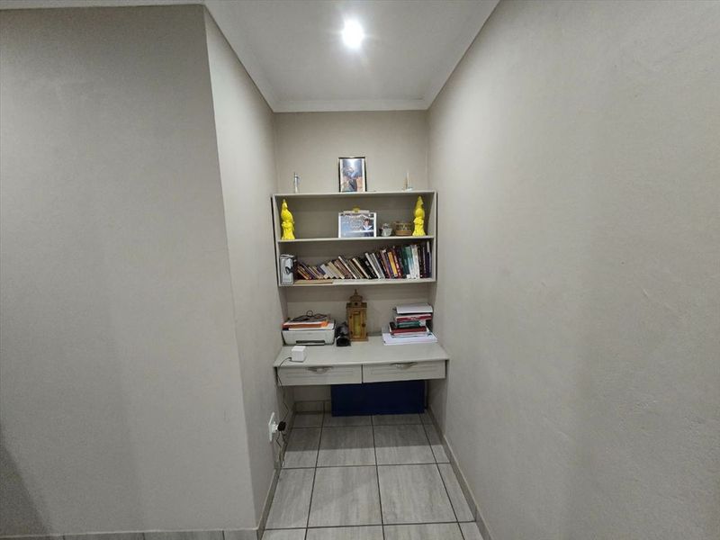 A compact built-in study nook featuring integrated desk space and shelving, finished with neutral wall tones and tiled flooring.