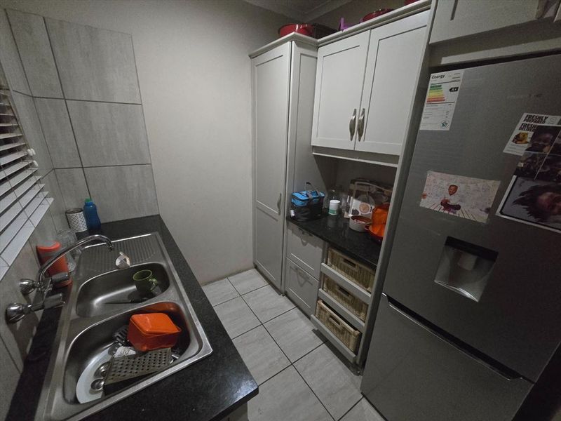A functional scullery featuring double basin sink, granite countertops, and ample built-in cabinetry with tiled flooring and splashback.
