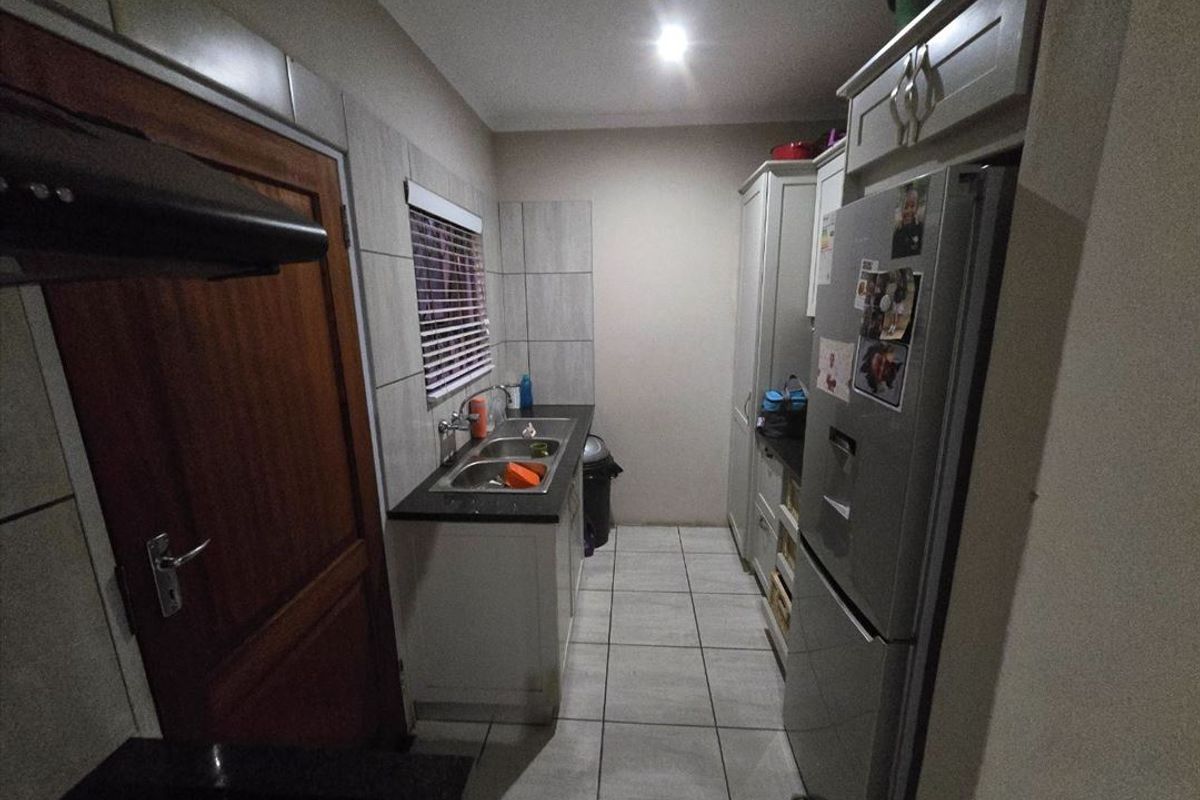 A functional scullery featuring built-in cabinetry, a double bowl sink, tiled splashbacks, and an extractor fan.
