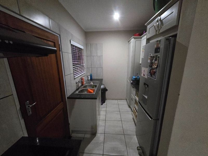 A functional scullery featuring built-in cabinetry, a double bowl sink, tiled splashbacks, and an extractor fan.