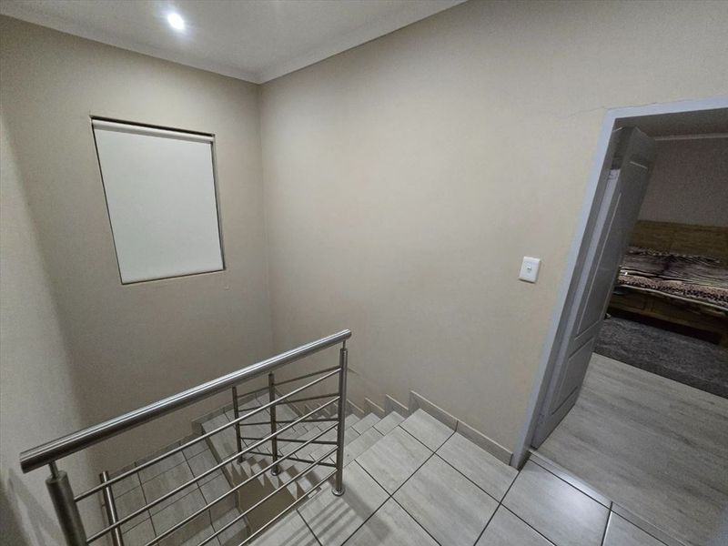A clean, modern hallway featuring tiled flooring and a stainless steel balustrade overlooking the staircase.