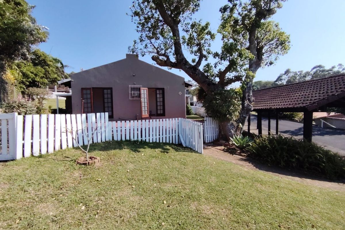 Exterior view of a townhouse featuring a private garden, white picket fencing, and a covered carport area.